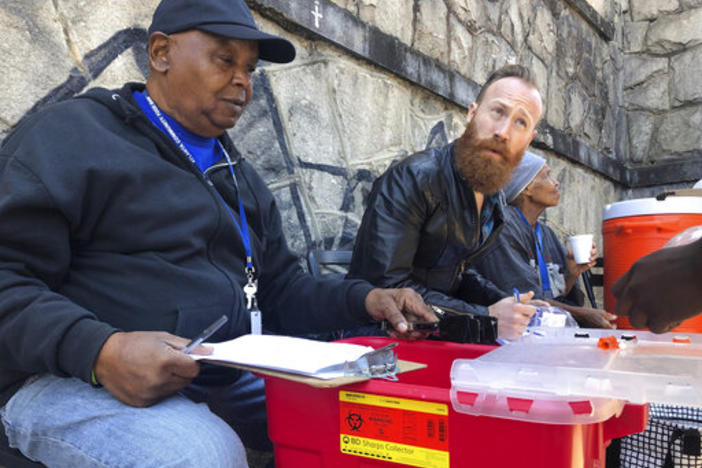 In this photo from March 20, 2019, Harry Ethridge, client services manager at the Atlanta Harm Reduction Coalition, and Jonathan Spuhler, an outreach coordinator for Absolute Care and volunteer at AHRC, set up a needle exchange station for drug users to swap out used syringes for clean syringes on English Avenue in Atlanta.