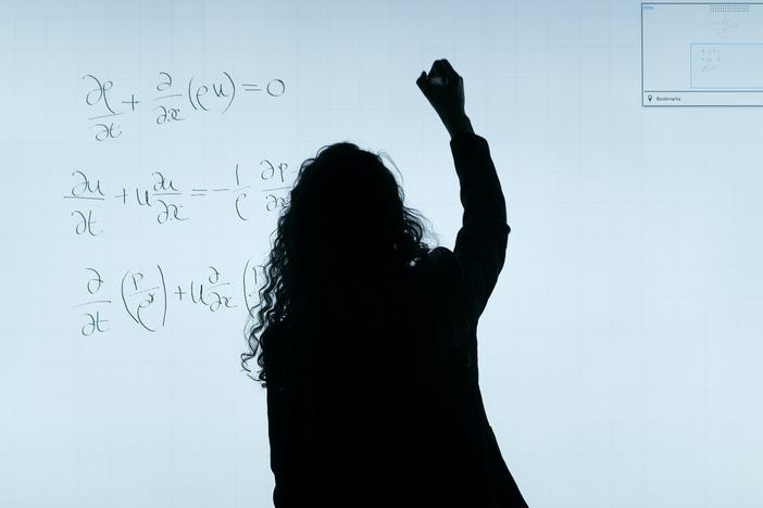 A backlit woman writes on a whiteboard
