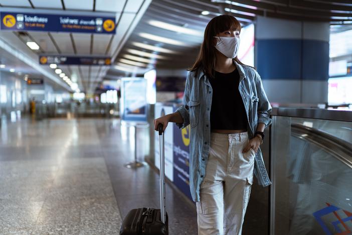 A woman in an airport wearing a face mask and holding luggage.