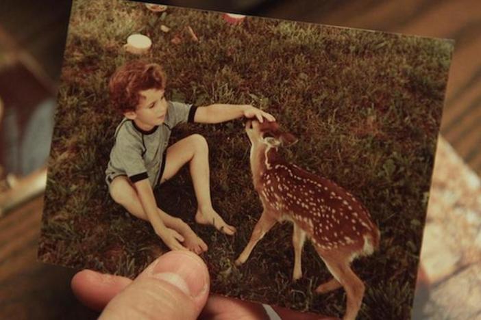 A person holds a picture of a child petting a fawn.