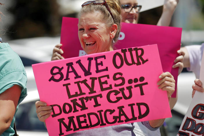 A woman holds a pink signs that says, "save our lilves ... don't gut medicaid"
