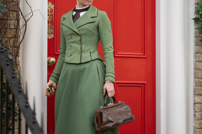 Miss Scarlet in period dress standing outside of a red door