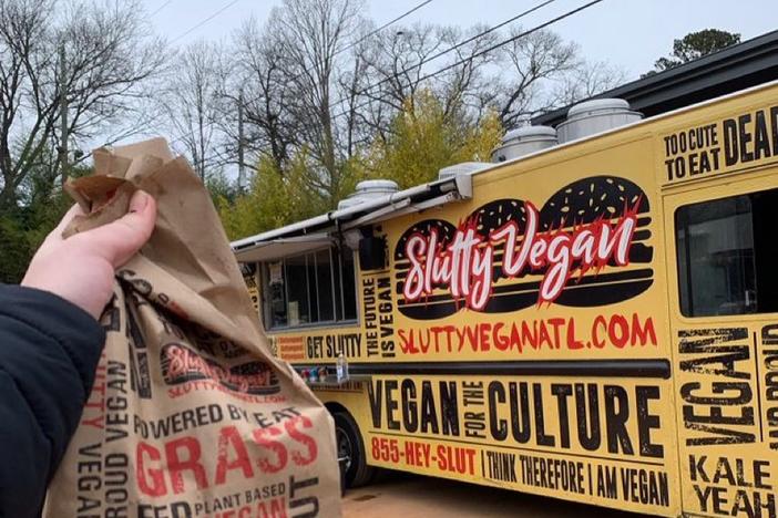 An outstretched arm holds a paper bag of food in front of the Slutty Vegan food truck in Atlanta.