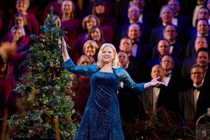 A woman in a blue gown standing in front of a choir and Christmas tree.