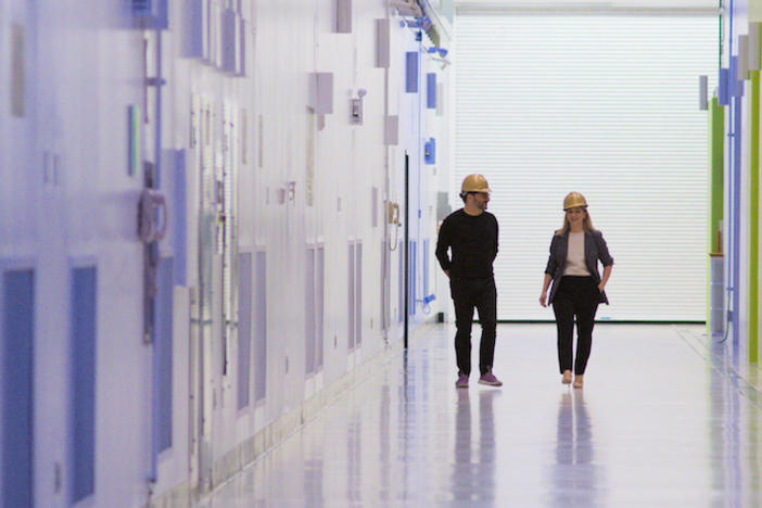 A man and woman in hardhats walking down a sterile corridor.