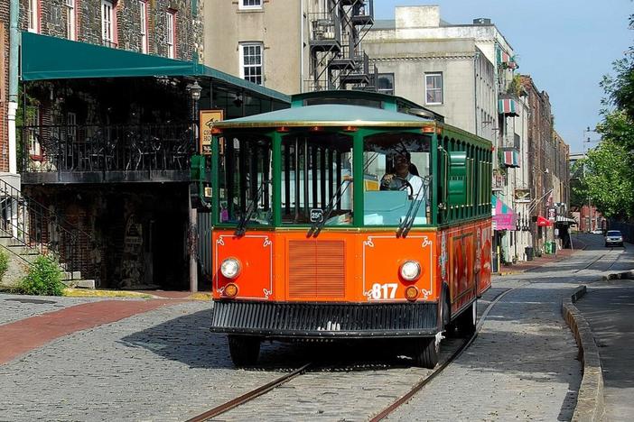 A trolley tour bus drives down River Street in downtown Savannah.