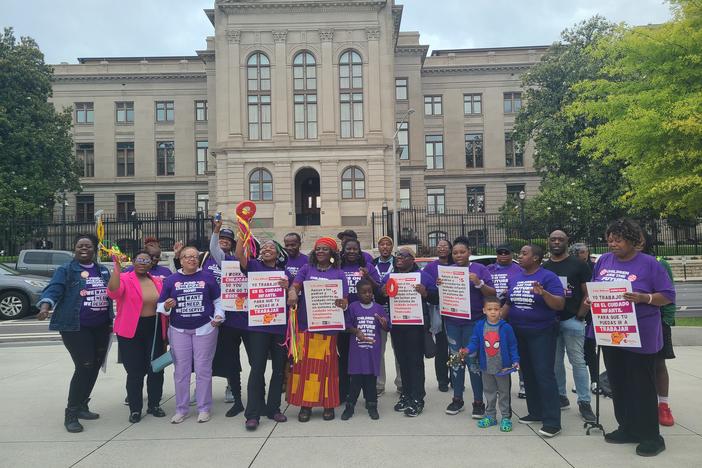 about 30 black people in purple shirts hold signs with a list of demands for better work conditions in front of the Georgia State Capitol.