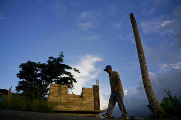 In this Sept. 8, 2018 photo, Ramon Alicea Burgos walks past his palm tree, with its top broken off one year ago by Hurricane Maria one outside his partially rebuilt home in the mountain town of Barranquitas, Puerto Rico. 
