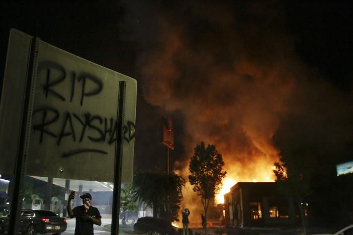 In this Saturday, June 13, 2020 file photo, "RIP Rayshard" is spray-painted on a sign as flames engulf a Wendy's restaurant where Rayshard Brooks was shot and killed by police in Atlanta.