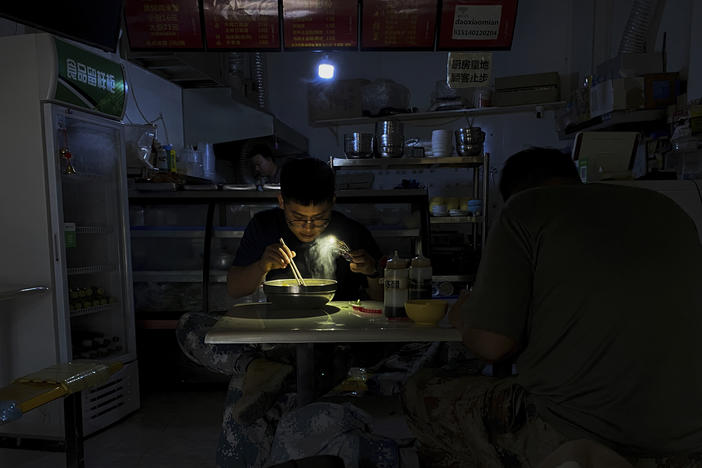A man uses his smartphone flashlight to light up his bowl of noodles as he eats breakfast at a restaurant during a blackout in Shenyang, in northeastern China's Liaoning province, Wednesday. People ate breakfast by flashlight and shopkeepers used portable generators as power cuts imposed to meet official conservation goals disrupted manufacturing and daily life.