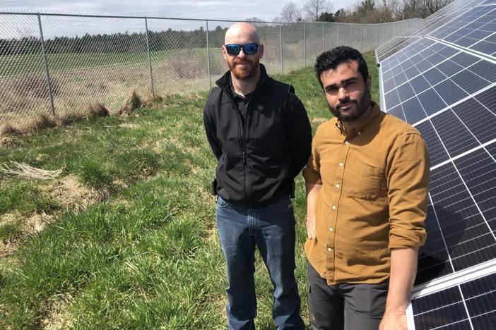 Adam Farkes and Leo Azevedo of BNRG at a solar energy project in Augusta, Maine. A bigger project planned on the far side of the fence is on hold because of a federal trade investigation.