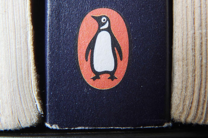 The Penguin logo is visible on the spine of a book. The U.S. Department of Justice is suing Penguin Random House and Simon & Schuster to block the companies from completing a merger valued at $2.175 billion.
