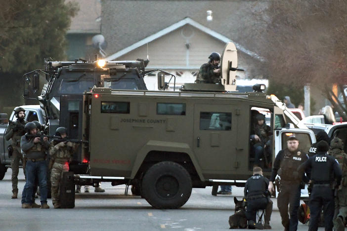 Law enforcement officers aim their weapons at a home during a standoff in Grants Pass, Ore., on Tuesday, Jan. 31, 2023. Police said the standoff involving a man suspected in a violent kidnapping in Oregon who was barricaded underneath the home had been "resolved."