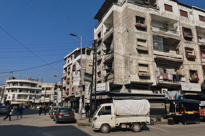 The city center of Jableh is home to older buildings as well as newer, less regulated construction. An image of President Bashar Assad hangs over a street cart with the slogan "We continue with you" in Arabic.