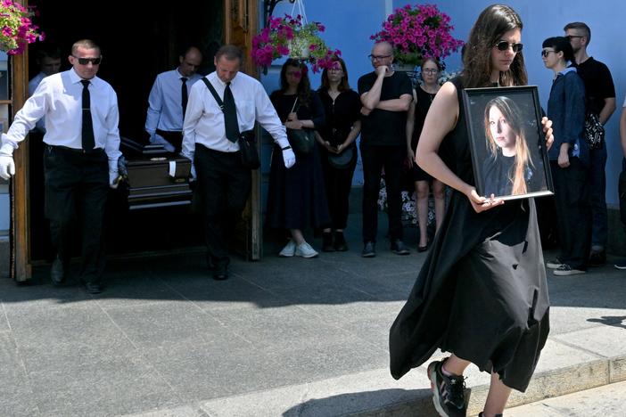 A woman holds a picture of Victoria Amelina, as pallbearers carry the writer's coffin at the end of her funeral ceremony in Mykhaylo Gold Domes in Kyiv on July 4, 2023.