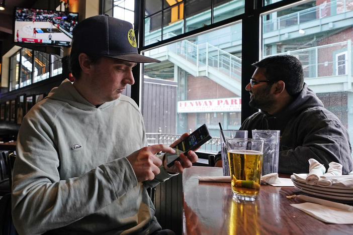 Taylor Foehl (left), of Boston, looks at a mobile betting app on his phone after placing a wager, while watching a men's college basketball game at the Cask 'N Flagon sports bar on March 10, 2023, near Fenway Park in Boston.