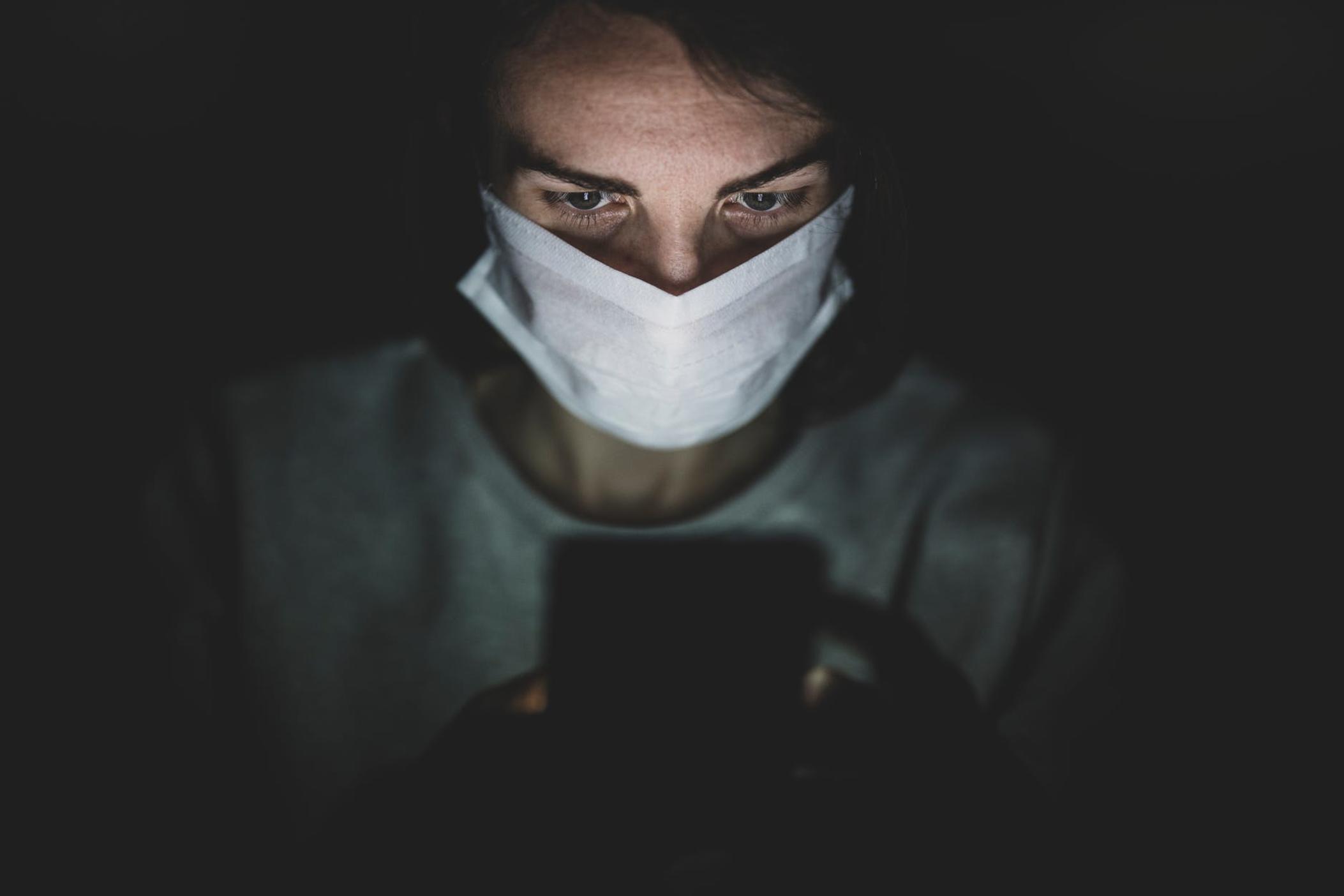 a person in a face mask looks at a phone screen.