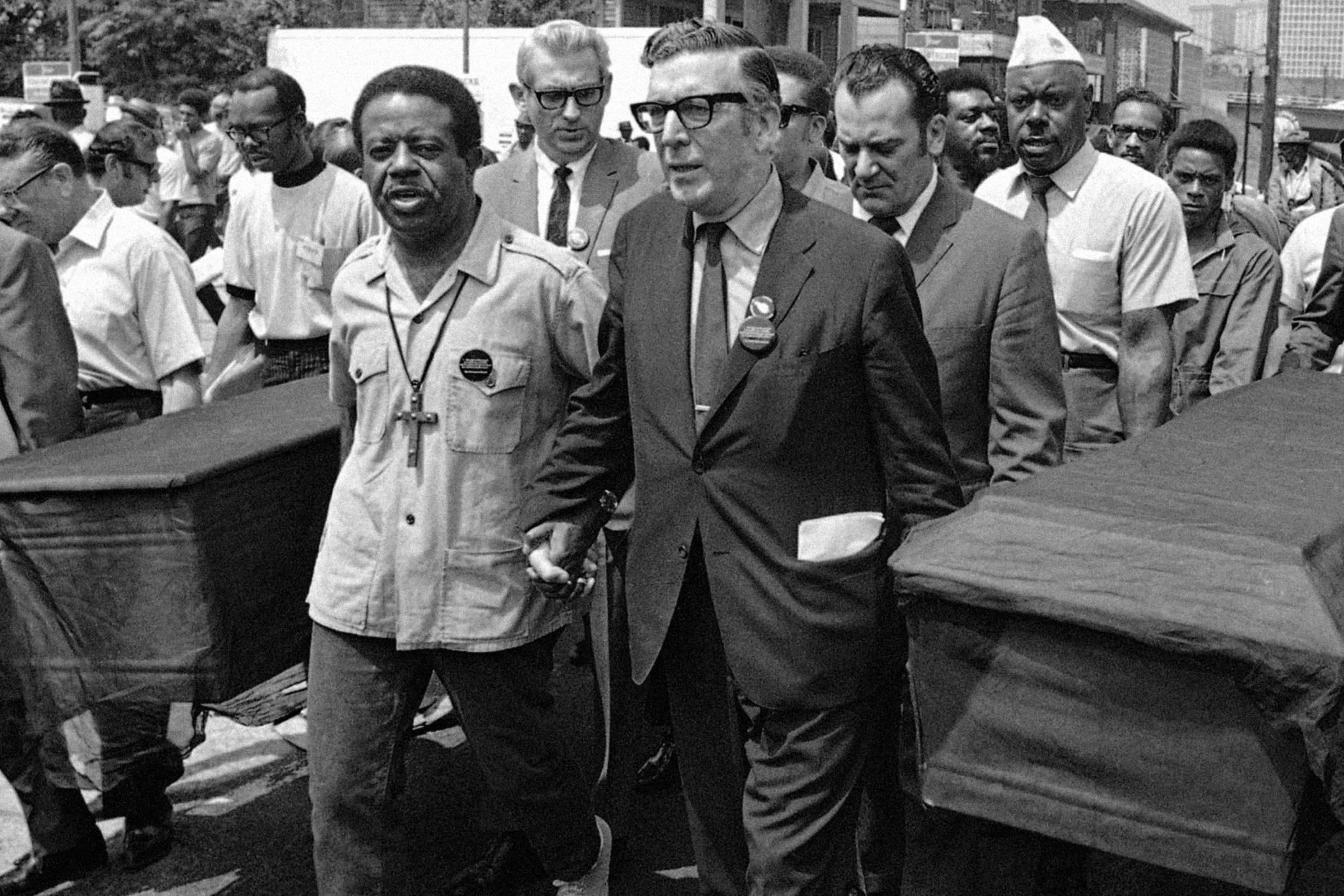 In this May 23, 1970 march in Atlanta, caskets are carried to protest the deaths of the six Black men shot in the back by police during the Augusta riot. Marchers also protested the deaths of students at Kent State University and Jackson State College. Pictured are Rev. Ralph Abernathy of the Southern Christian Leadership Conference (center left), and Leonard Woodcock of the UAW union (center right).