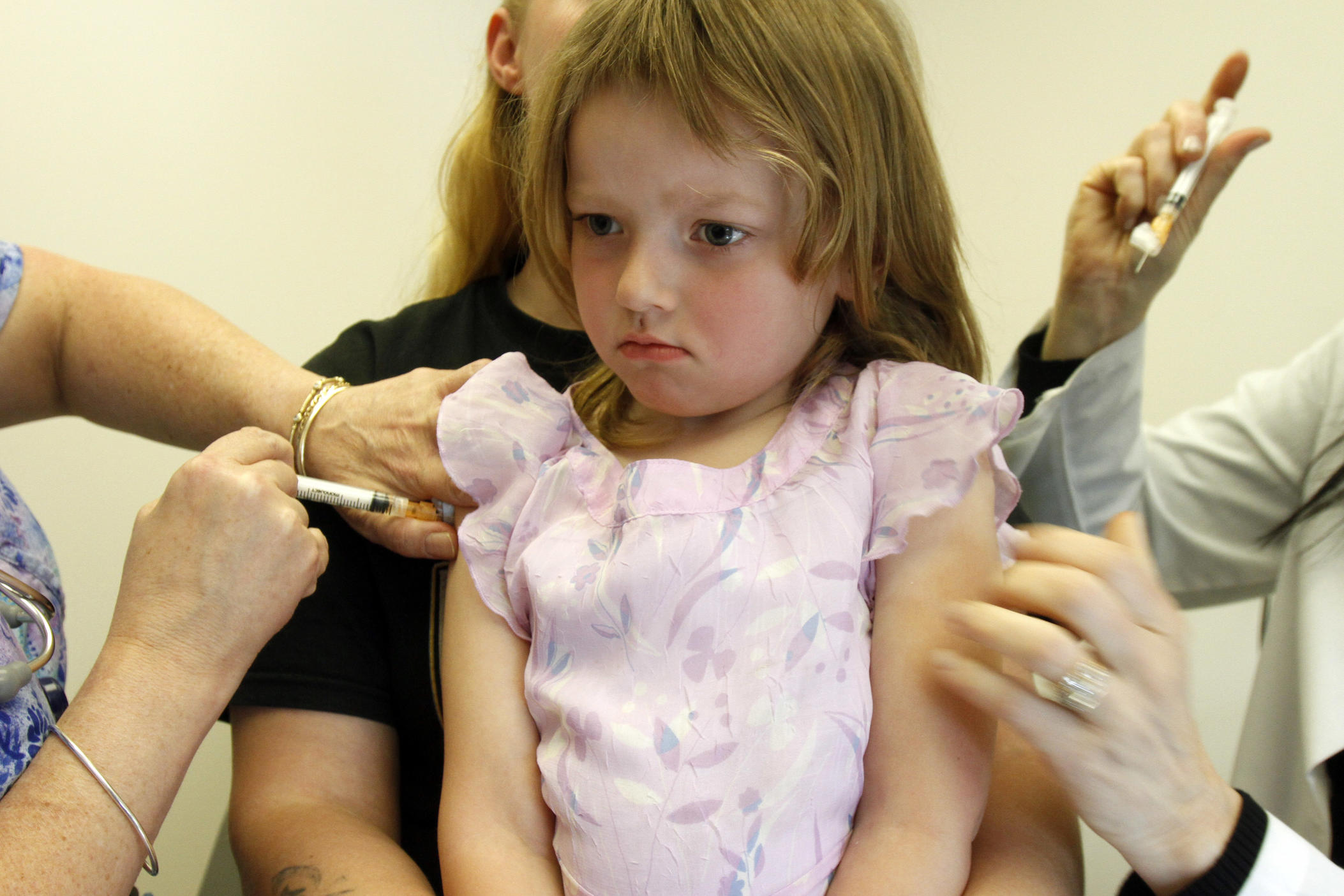 A young girl gets a vaccine in her right shoulder