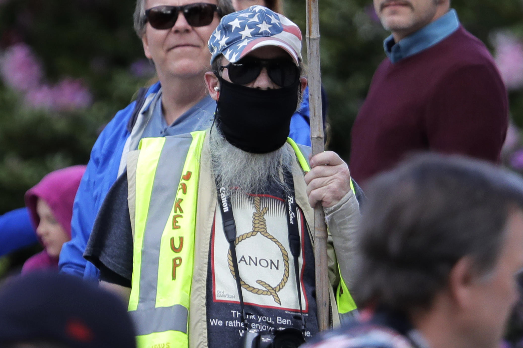 In this May 14, 2020, photo, a person carrying a sign supporting QAnon wears a t-shirt that shows the QAnon name in the format of a rope noose during a protest rally in Olympia, Wash., held against Gov. Jay Inslee and Washington state stay-at-home orders made in efforts to prevent the spread of the coronavirus.