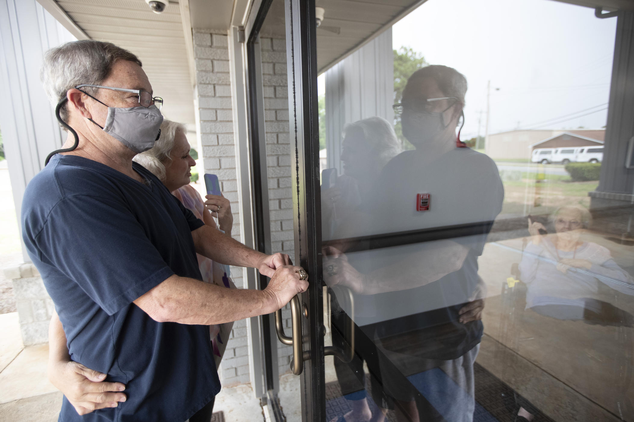 Southern Pines nursing home resident Shirley Campbell visits with her daughter, Margie Price, and son-in-law, Ken, through a glass door in Warner Robins, Ga., on Friday, June 26, 2020. A state emergency order barring nursing home visits has been extended another month to Aug. 12. With Georgia recording a sharp spike in virus cases, residents and staff alike know another delay is possible. 