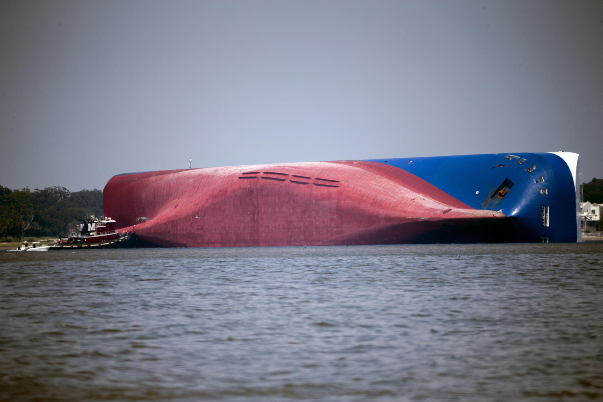 FILE - In this Sept. 9, 2019, file photo, a Moran tugboat nears the stern of the capsizing vessel Golden Ray as a tent and rescuers can be seen near the bottom of the ship near the tug boat in Jekyll Island, Ga. Marine salvage experts are trying to determine what caused a fire, Sunday, Oct. 20, in the overturned cargo ship lying close to Georgia's seacoast. (AP Photo/Stephen B. Morton, File)