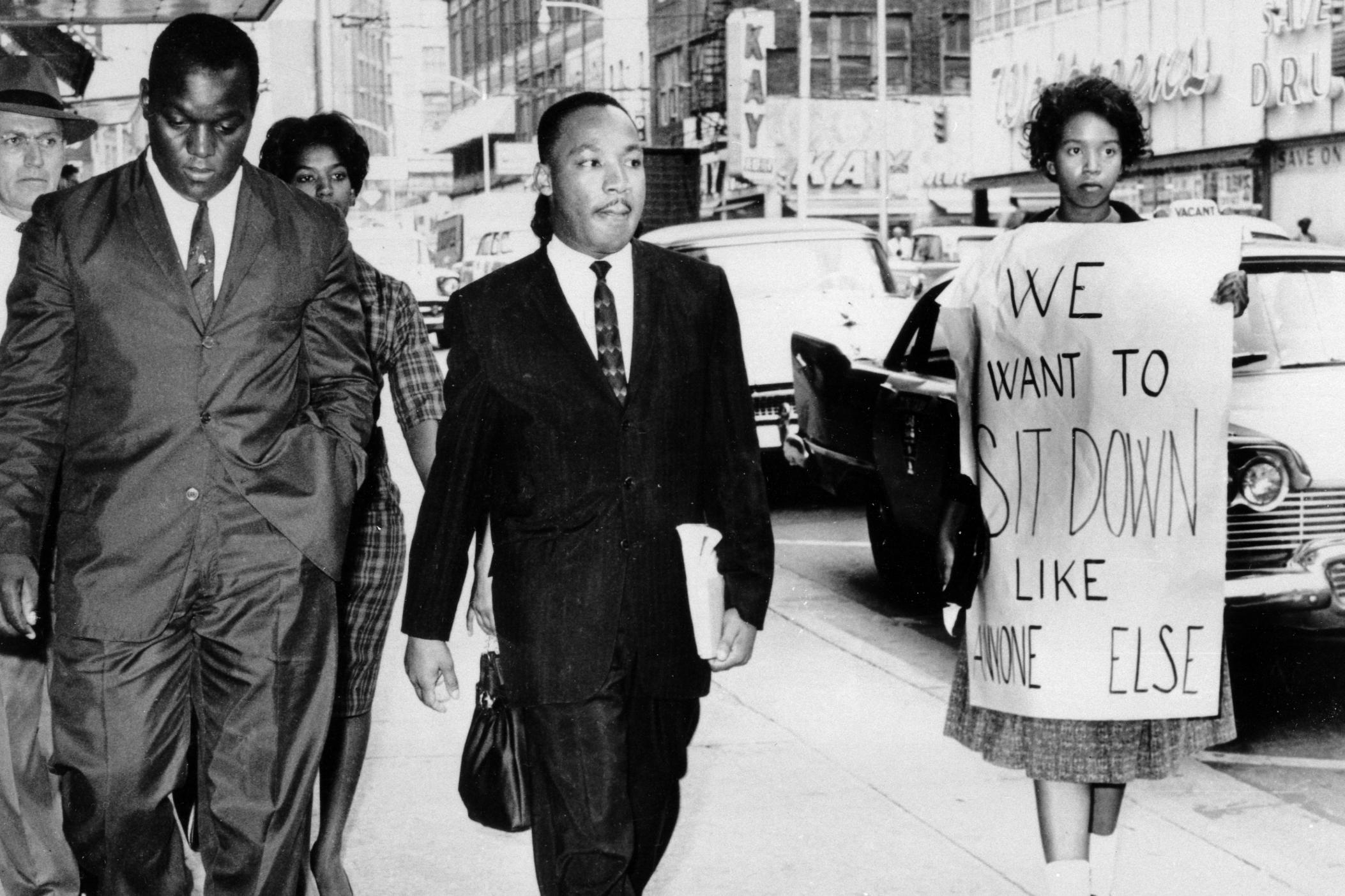 In this Oct. 19, 1960 file photo, Dr. Martin Luther King Jr. under arrest by Atlanta Police Captain R.E. Little, left rear, passes through a picket line outside Rich's Department Store, in atlanta.