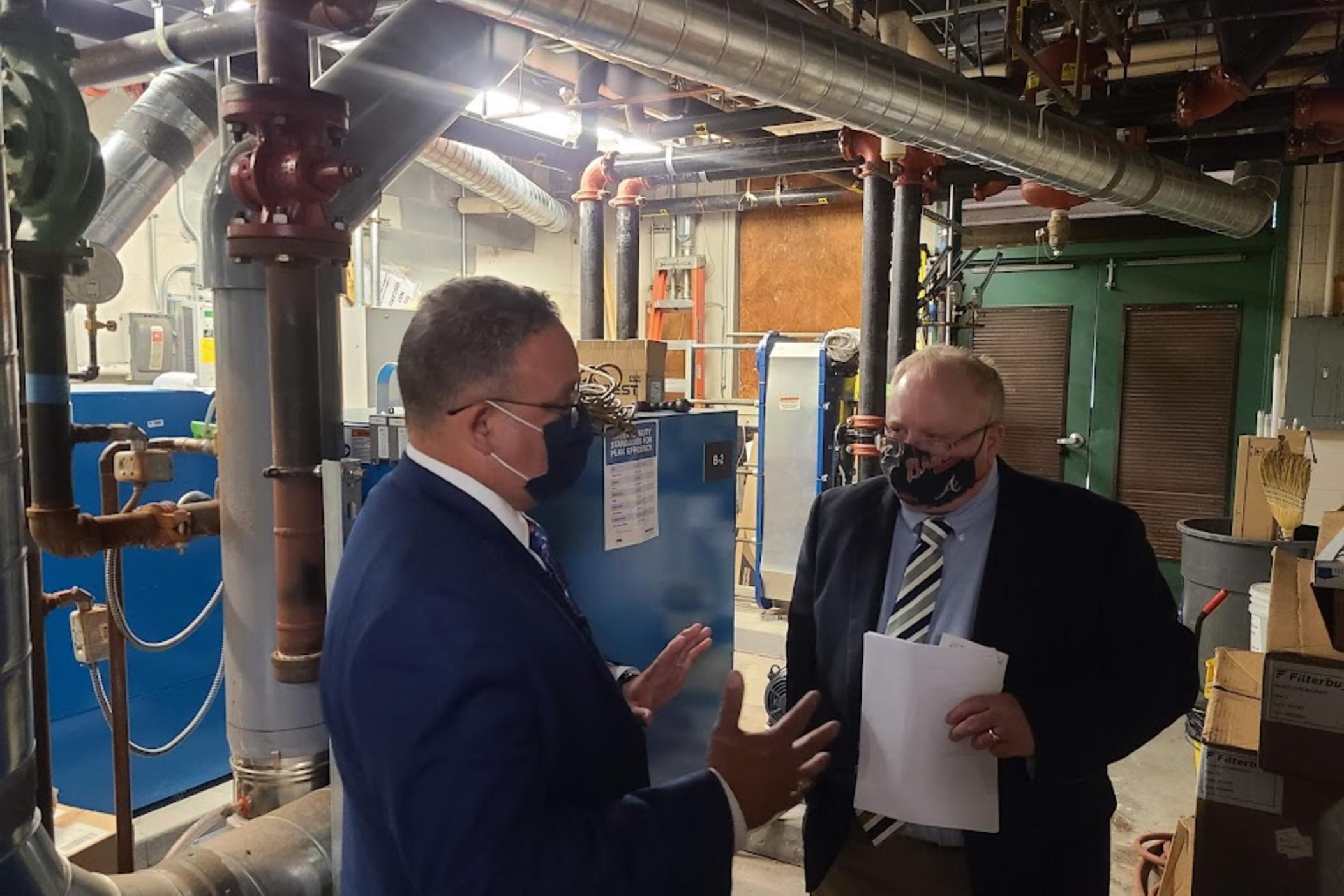 U.S. Secretary of Education Miguel Cardona (left) speaks to the operations manager of Kelley Lake Elementary in the boiler room about ventilation changes during a visit to the DeKalb County school Friday, July 23, 2021.