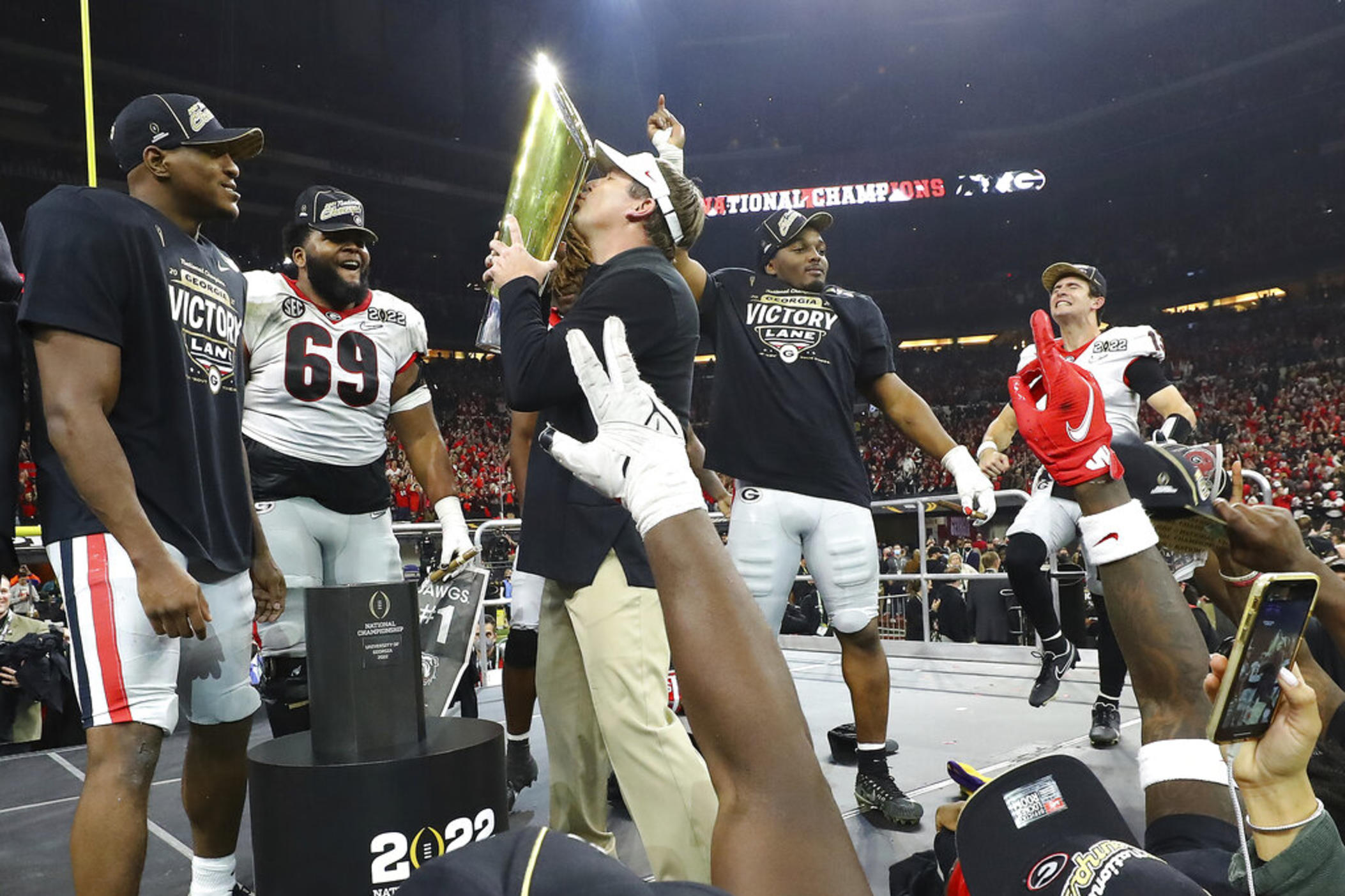 Georgia head coach Kirby Smart kisses the trophy while Zamir White (from left) Jamaree Salyer, Nakobe Dean and quarterback Stetson Bennett celebrate on stage winning the College Football Playoff Championship game over Alabama, early Tuesday, Jan. 11, 2022, in Indianapolis.
