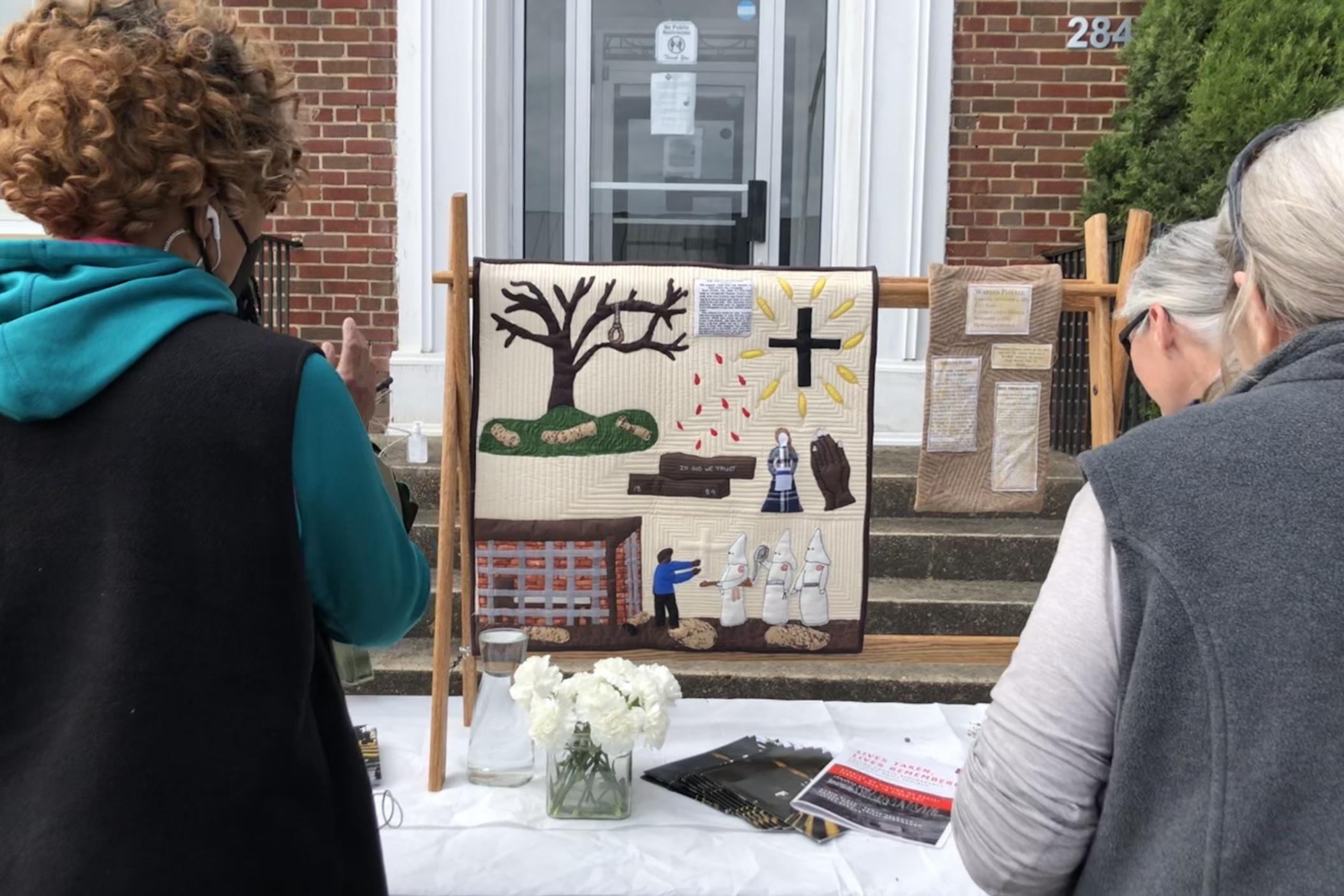 Attendees look at a quilt made by local artist Robin Black of the Remembrance Quilters in honor of 1889 lynching victim Warren Powell.