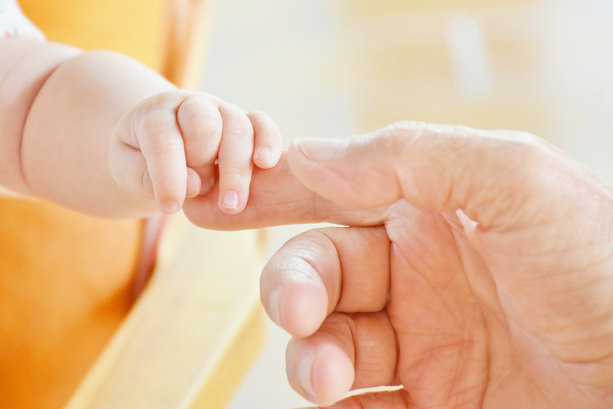 Image shows a baby's hand holding an adult index finger.