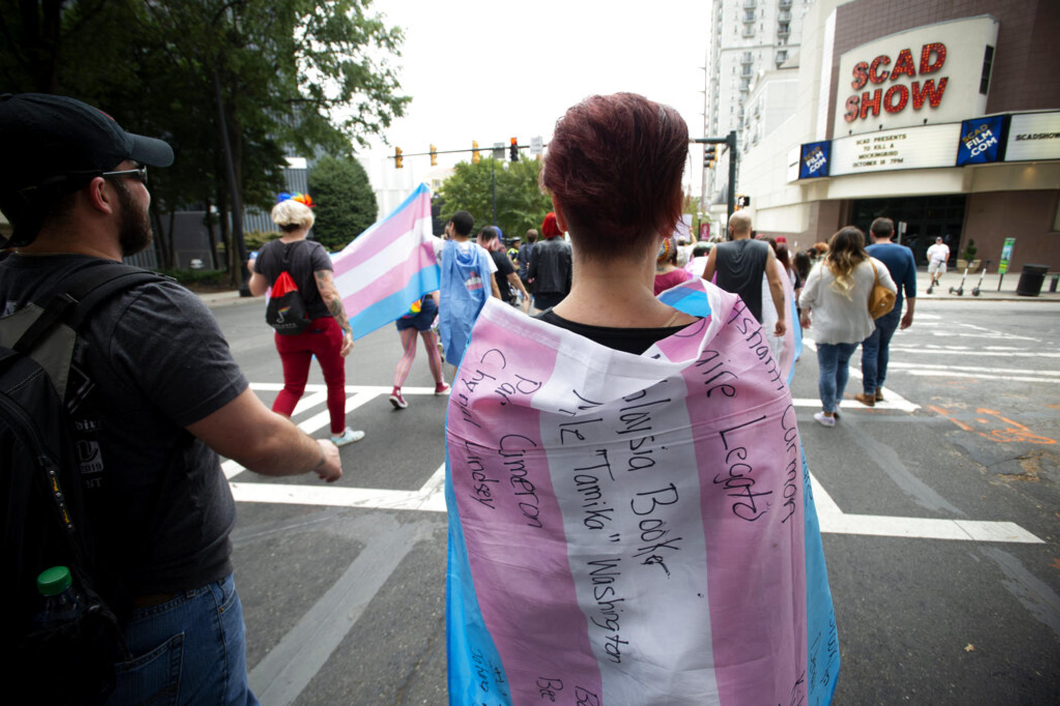A supporter for the transgender and non-binary community, wearing a transgender flag with handwritten names of black trans women who the person said were killed in 2019, strolls through the city's Midtown district during Gay Pride Festival's Transgender Rights March in Atlanta on Saturday, Oct. 12, 2019. The march was part of the annual Gay Pride Festival. (AP Photo/Robin Rayne)