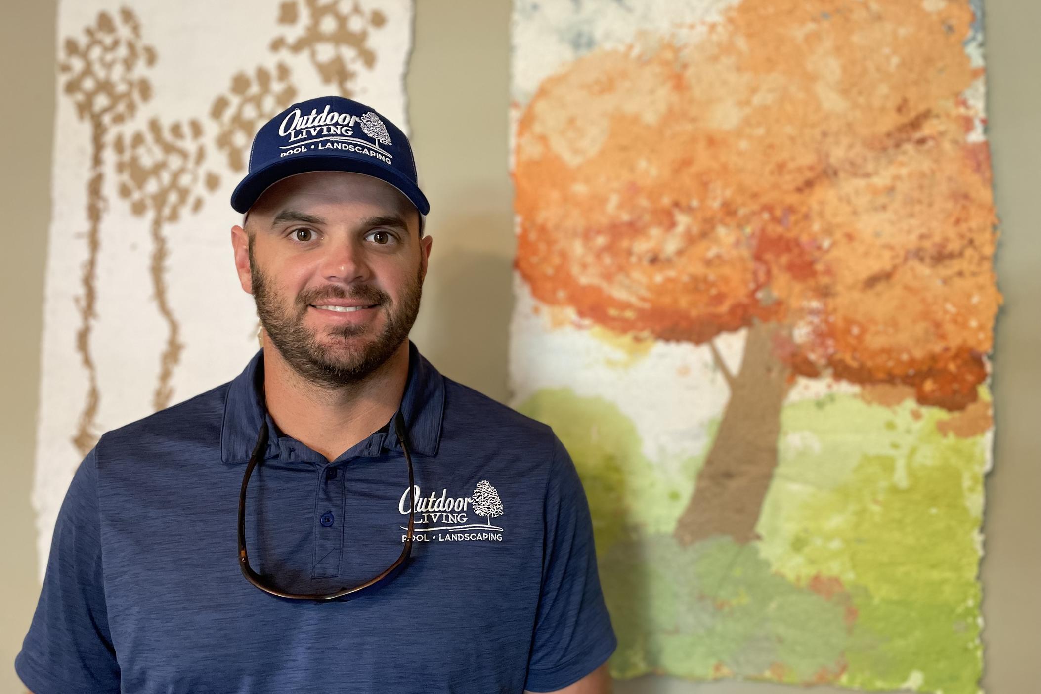 Brent Moore stands in front of a painting of a tree