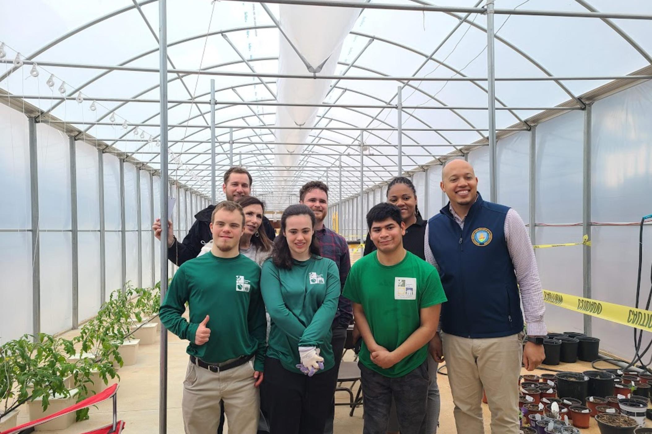 John, Qwen, and Joey wearing the green Peachtree Farms uniform stand in the greenhouse on the farm.