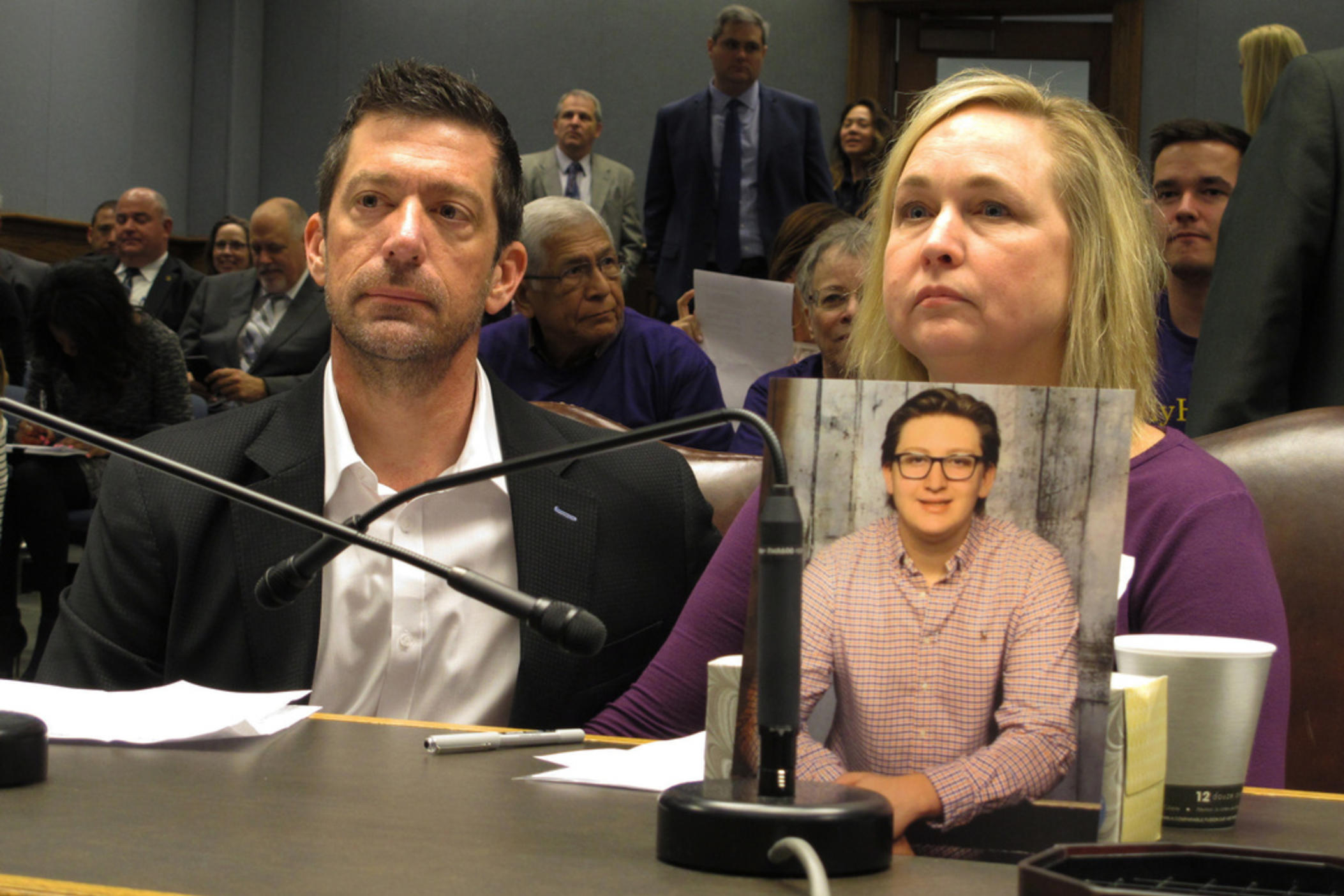 Stephen and Rae Ann Gruver sit in a House committee room behind a photo of their son, 18-year-old Maxwell Gruver, a Louisiana State University freshman who died with a blood-alcohol content six times higher than the legal limit for driving in what authorities say was a hazing incident, in Baton Rouge, La., on March 21, 2018. 