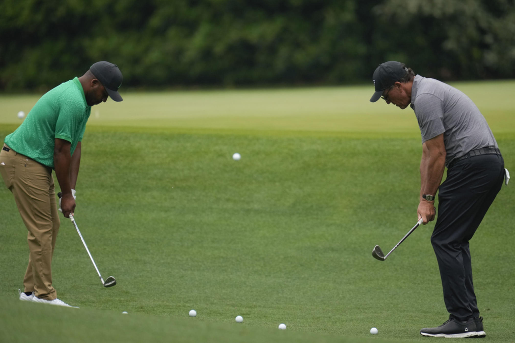 Harold Varner III, left, and Phil Mickelson chip to the 11th green during a practice for the Masters golf tournament at Augusta National Golf Club, Tuesday, April 4, 2023, in Augusta, Ga.