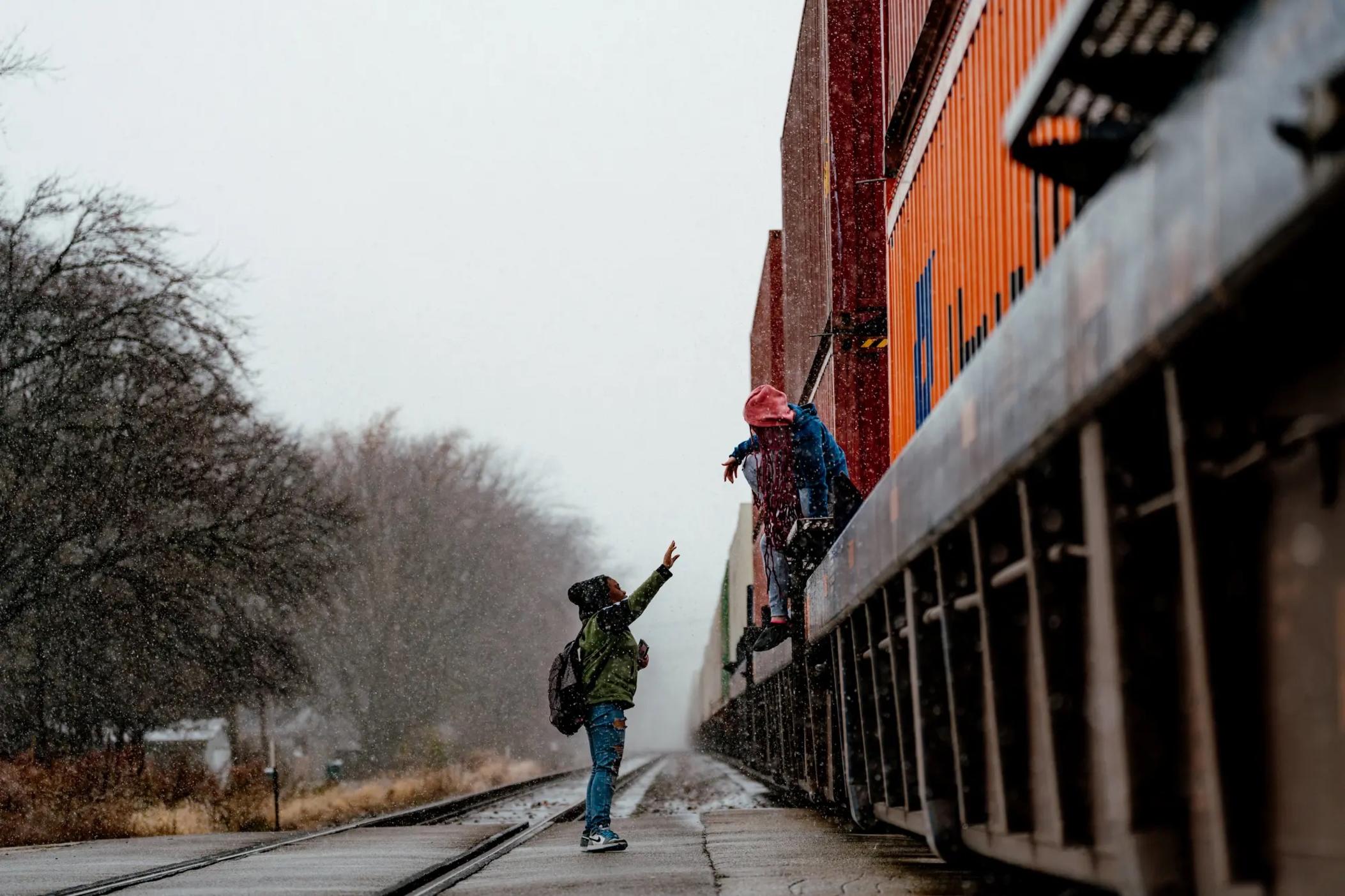  One child helps another cross over a parked freight train blocking their route to school. 