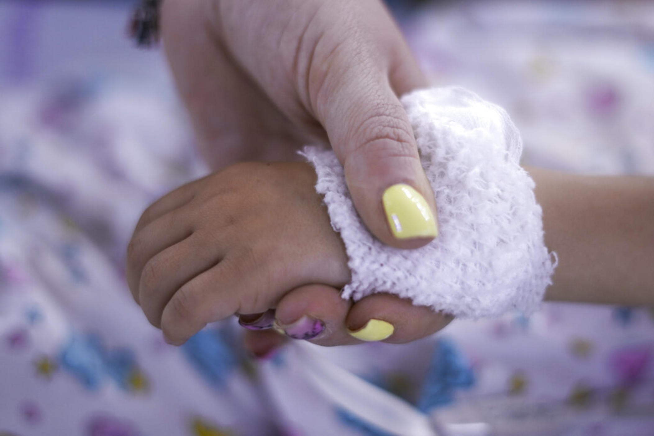an adult hand holds a bandaged newborn hand