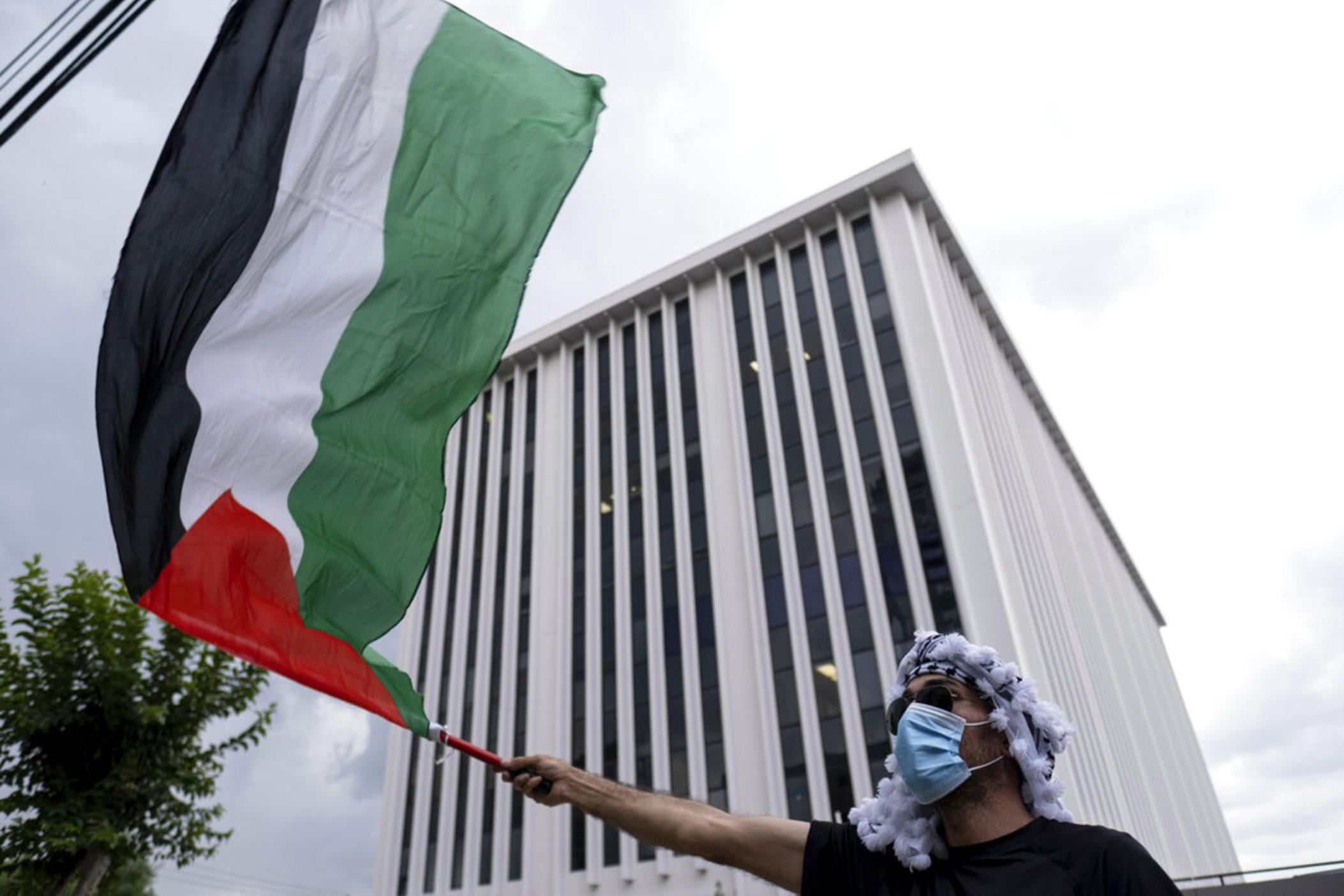 A pro-Palestinian protester waves a flag in front of the building housing the Israeli Consulate office in Atlanta on Tuesday evening, May 18, 2021. 