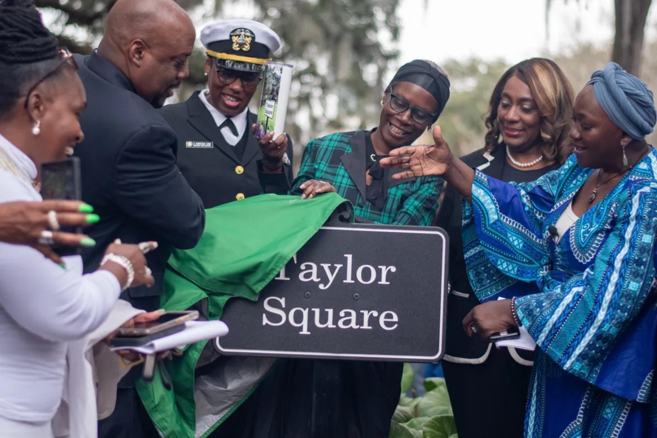 Mayor Van Johnson pulls back the cover on the new sign for Taylor Square along with Patt Gunn, right in blue, along with city council members and others unveiled the sign for Taylor Square. Credit: Jeffery Glover/The Current