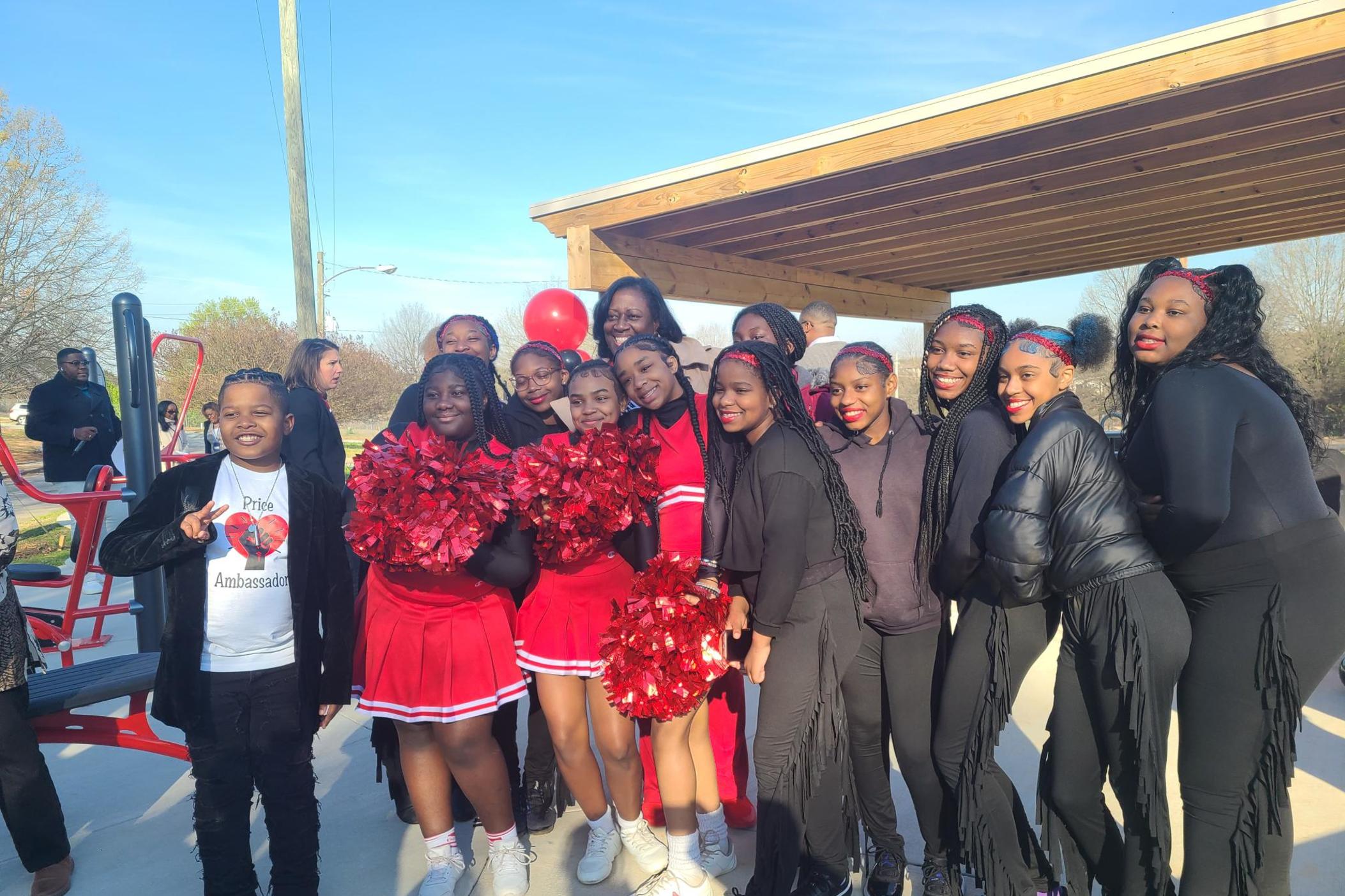 Students from Luther J. Price Middle School in Southeast Atlanta pose with Atlanta Public Schools Interim Superintendent Danielle S. Battle at the ribbon-cutting ceremony for a new community park on March 20, 2024. Four girls wear red cheer uniforms another four wear black majorette uniforms.
