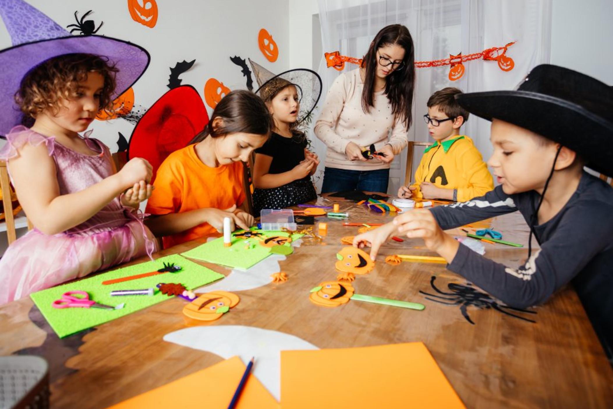 Teacher and students make paper jack-o-lanterns at a table.