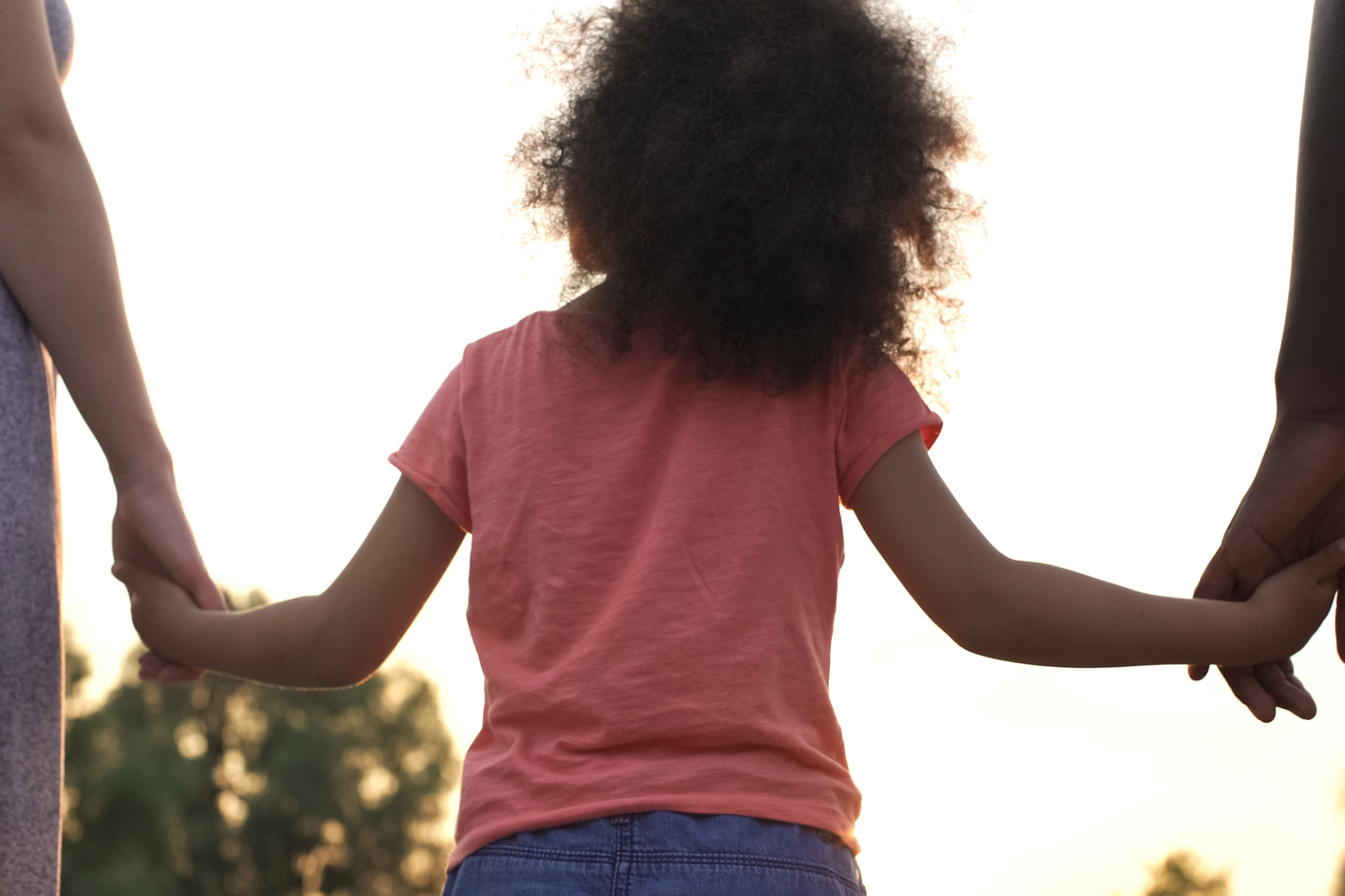 little girl holds hands with her parents 