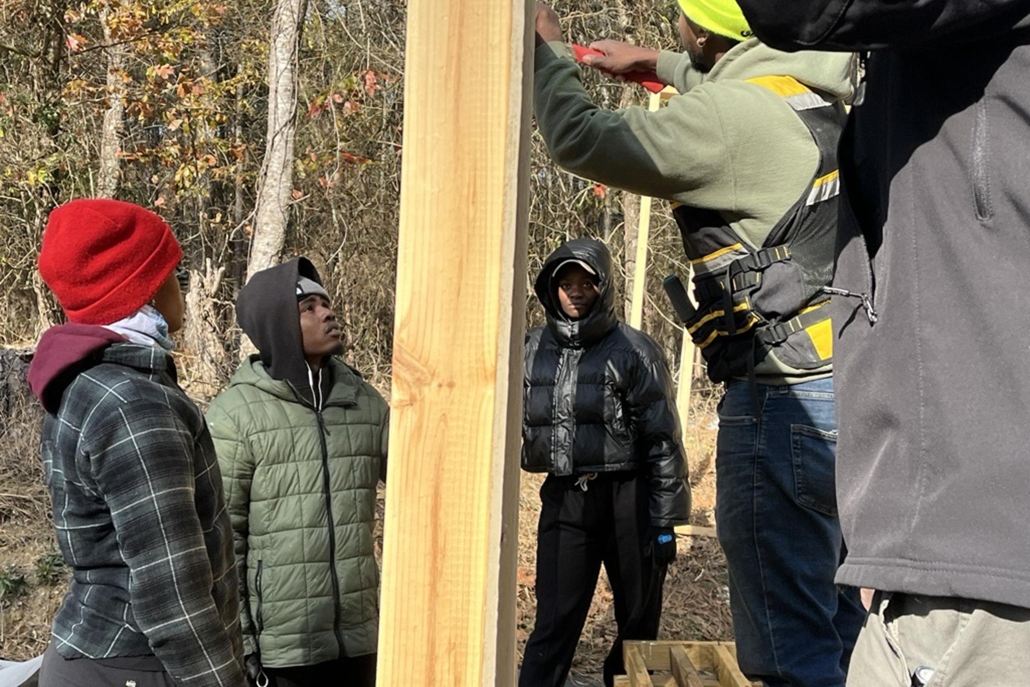 Students in the g2g program hold up a wall as part of a shed building project