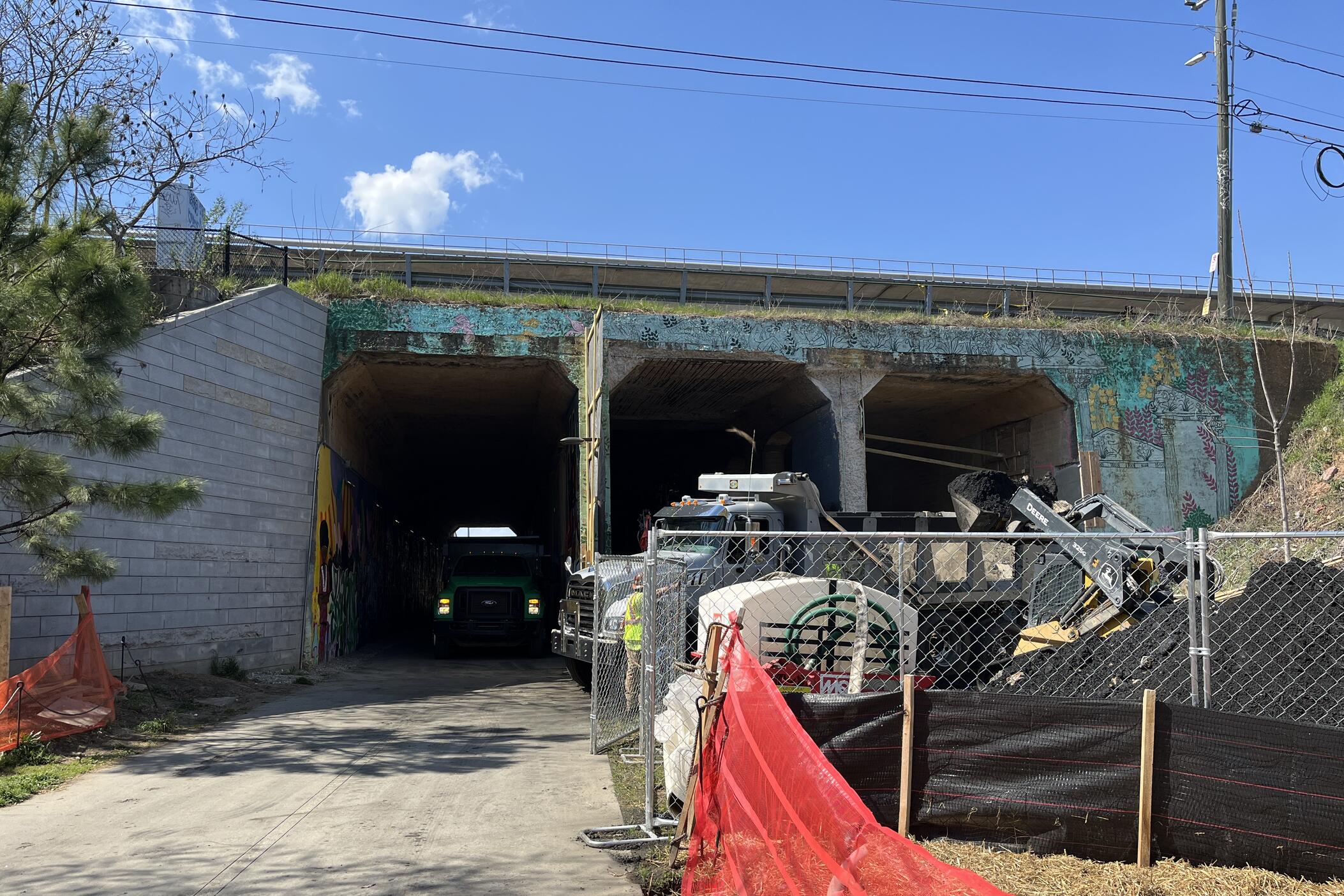 Three tunnels under a train track. One has a path going through it, while the other two are blocked by construction.