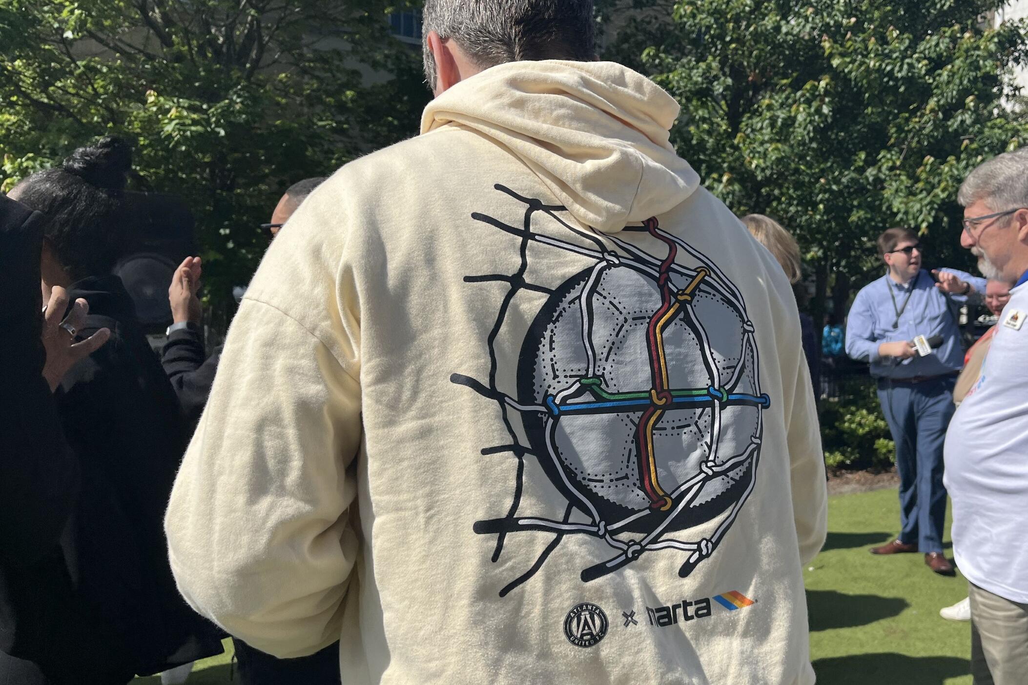 A cream color hoodie where the soccer ball hits a net and the net forms the shape of the MARTA transit lines