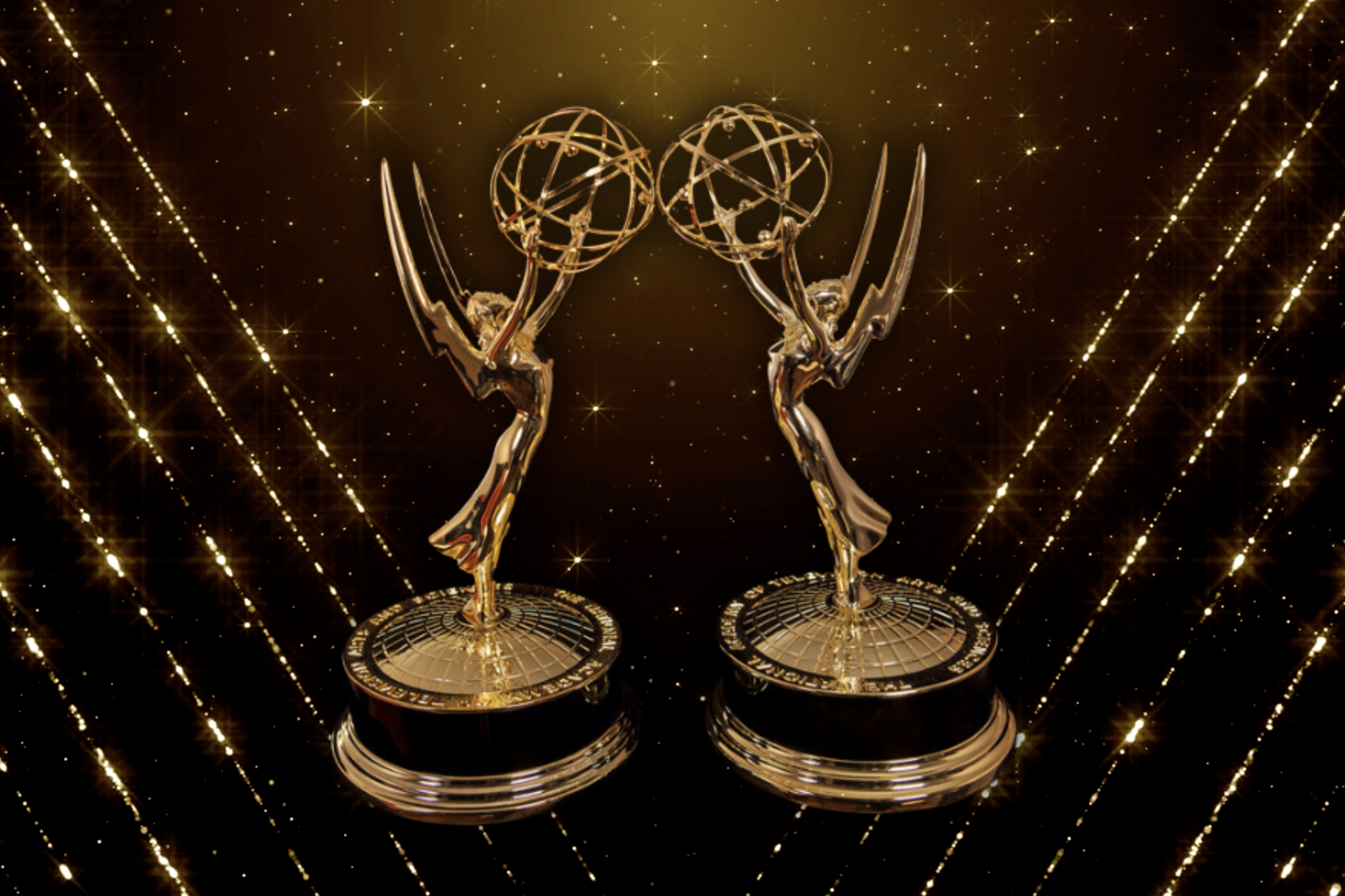 Two Emmy statuettes on top of a glittery background. 