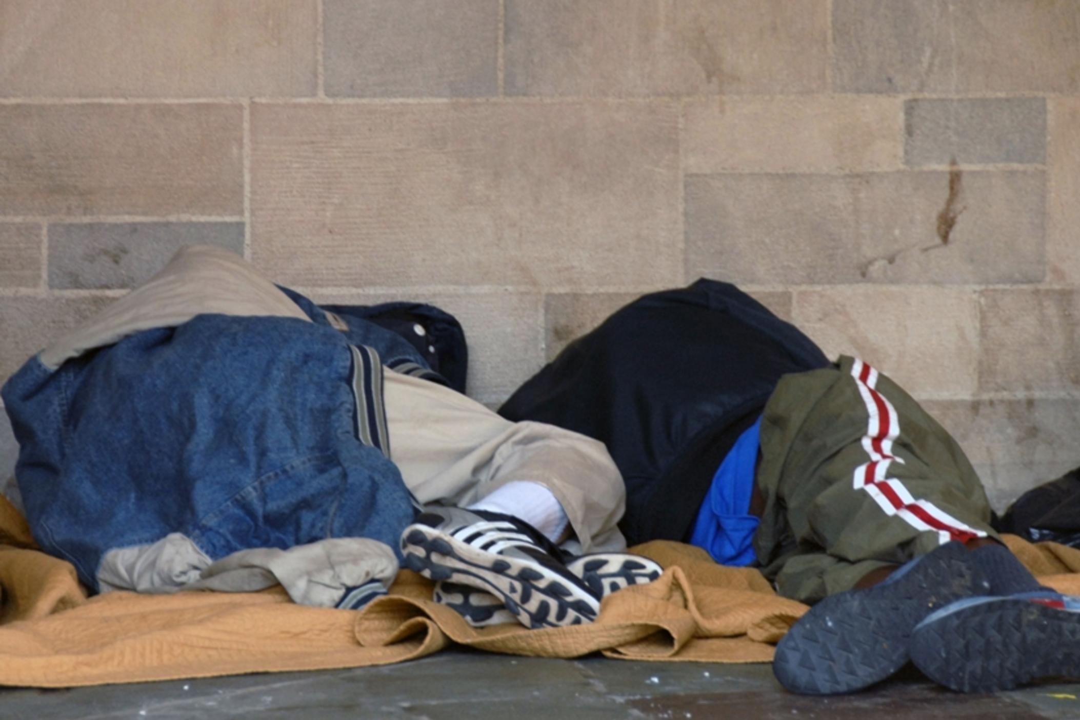 Homeless individuals rest against a wall