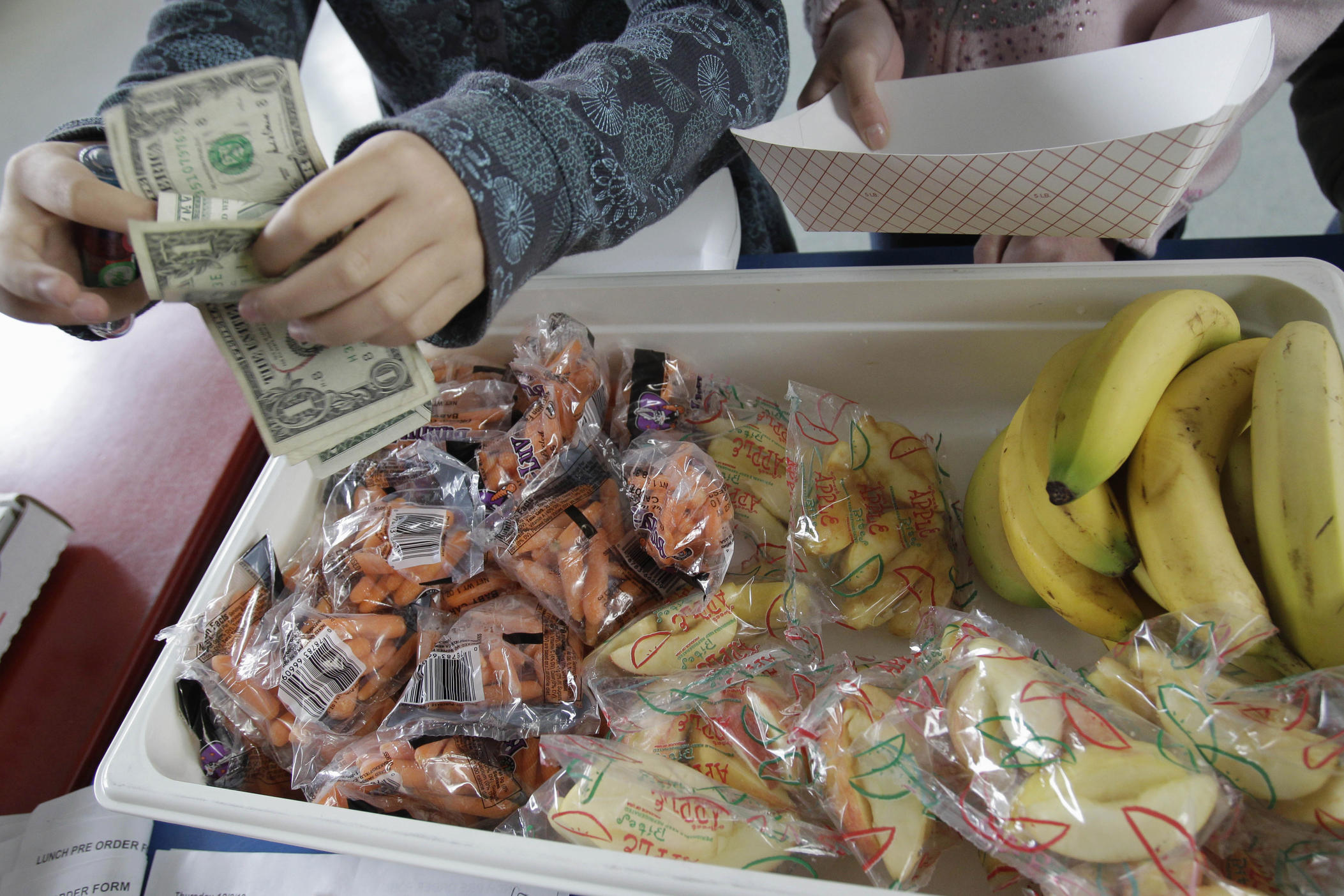 A student pays for a lunch of fruits and vegetables as part of a school lunch program.
