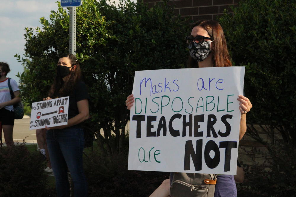 A woman in a mask holds a sign that says "Masks are disposable, teachers are not."